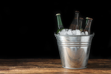 Metal bucket with bottles of beer and ice cubes on wooden table. Space for text