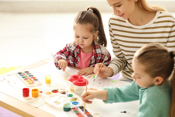 Mother and daughters painting at table indoors. Playing with children