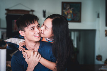 Asian young couple is smiling in love, Beautiful woman kiss and hugging handsome man from the back in the room, Happy cheerful family.