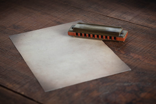 Vintage Harmonica With A Old Paper In A Wood Table