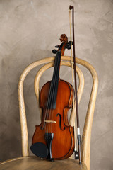 Fototapeta na wymiar Classic violin and bow on chair against beige background