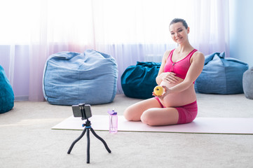 A pregnant woman does gymnastics live. The expectant mother shoots a video of training on mats for her blog. Last trimester.