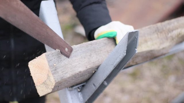 A human is sawing a log with a hand saw in the street on a stand. Logging firewood.