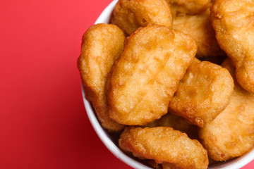 Bucket with delicious chicken nuggets on red background, top view