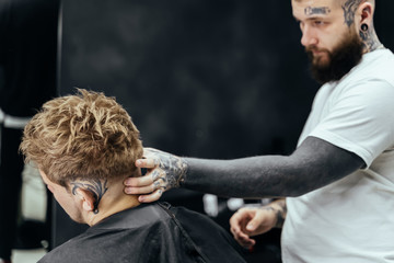 Barber makes hair styling with hair gel and comb after haircut at the barber shop. Young handsome Caucasian man getting a haircut in a modern hairsalon
