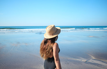 beautiful woman in a brown hat and black bikini enjoying the beach