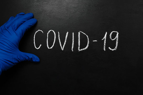 Coronavirus concept. The inscription in white chalk on a black slate background and a blue medical sterile glove. Epidemic of coronavirus infection. Pandemic. place for text or image placement