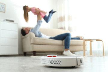 Man and his daughter having fun while robotic vacuum cleaner doing its work at home
