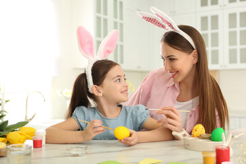 Happy mother and daughter with bunny ears headbands painting Easter egg in kitchen