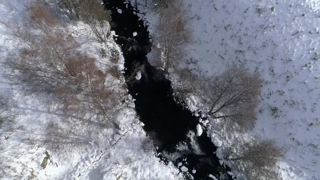 AERIAL DRONE TOP DOWN CLOSE SHOT FOLLOWING FROZEN RIVER CROSSING SNOWED FIELDS AND FOREST
