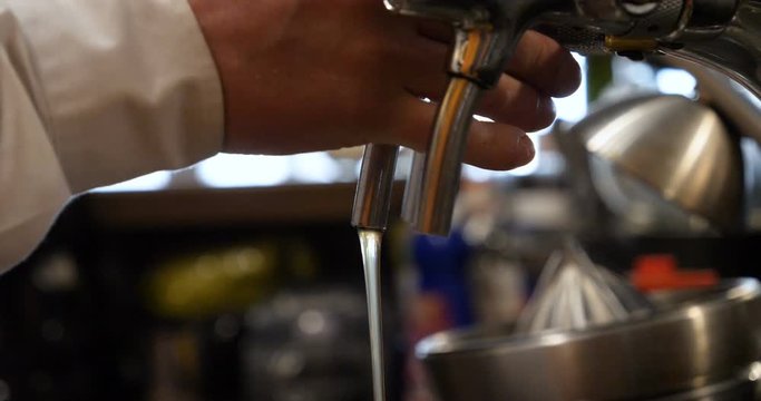 Barman hand at beer tap pouring a draught lager beer serving in a restaurant or pub.