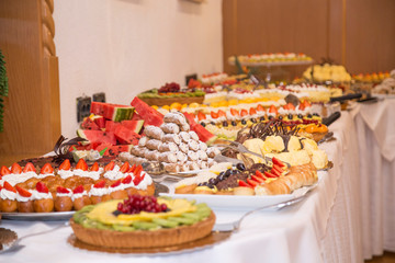 buffet with sweets. fruits and other sweets on dessert table. Rows of tasty looking desserts in beautiful arrangements. Sweets on banquet table - picture taken during catering event
