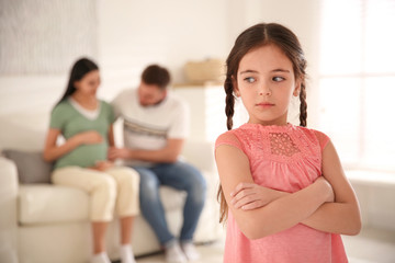 Unhappy little girl and her father with pregnant mother at home. Feeling jealous towards unborn sibling