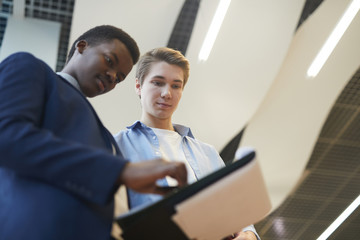 Low angle portrait of two young businessmen discussing work project while standing in office, copy space
