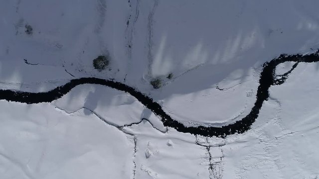 AERIAL DRONE TOP DOWN SIDE SHOT FOLLOWING FROZEN RIVER CROSSING SNOWED FIELDS