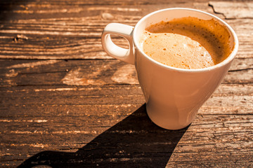 A cup of cappuccino in white cup isolated on wooden table background In sunlight