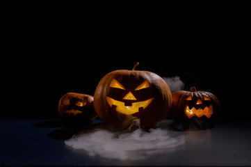 Halloween card. jack o lantern with candles glow on a black background. A row of creepy pumpkins with carved grimaces smokes in the dark.