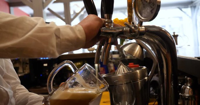 Barman hand at beer tap pouring a draught lager beer serving in a restaurant or pub.