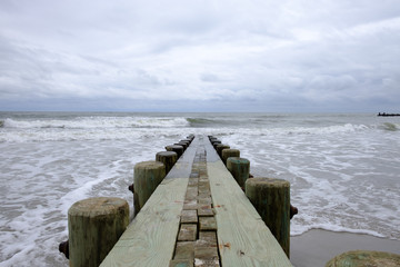 Isolated pier jetty with ocean and sky background. Waves crashing on beach wooden jetty pier. 