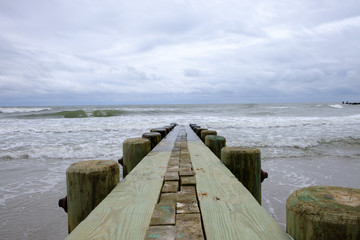 Isolated pier jetty with ocean and sky background. Waves crashing on beach wooden jetty pier.  - 348353869