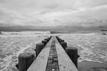 Isolated pier jetty with ocean and sky background. Waves crashing on beach wooden jetty pier.  - 348353873