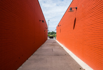 Street photography of abstract long alleyway. Pathway between two buildings with red brick wall facade. Minimal street photography. Light and shadow on brick wall exteriors.   - 348354034