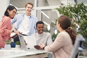 Multi-ethnic group of young business people discussing work project and smiling cheerfully during...