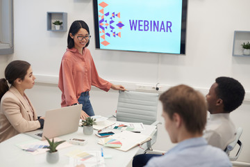 Portrait of young Asian woman smiling cheerfully while giving presentation during business seminar...
