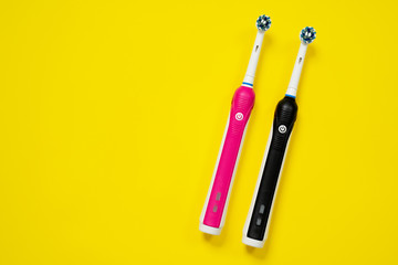 Pair of pink for girl and black for boy electric toothbrushes with replacement heads, top view, copy space.
