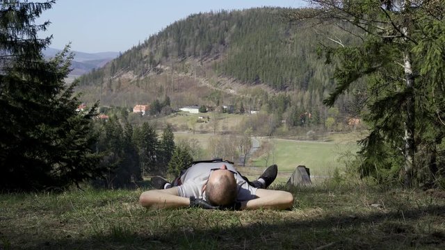 A young man resting after work lying in a meadow, beautiful hills and woods visible in the background. Polish wild nature, Karkonosze mountains. Lower Silesia, Poland.