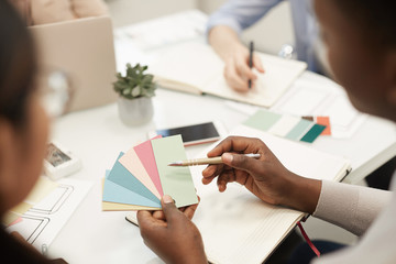 Close up of unrecognizable African-American man holding color swatches while discussing design project with colleagues during meeting in office, copy space