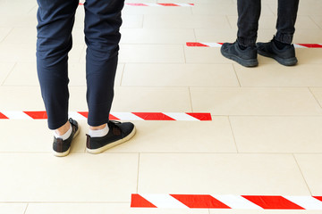 People stand in line keeping social distance, standing behind a warning line during covid 19 coronavirus quarantine. Safe shopping, Social distancing concept. Legs in line close up - Powered by Adobe