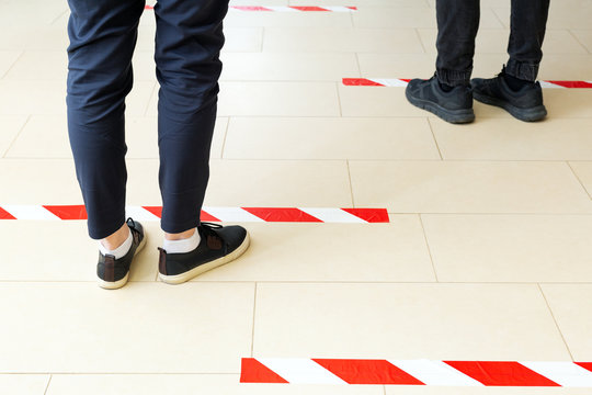 People Stand In Line Keeping Social Distance, Standing Behind A Warning Line During Covid 19 Coronavirus Quarantine. Safe Shopping, Social Distancing Concept. Legs In Line Close Up