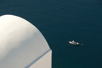 A fishing boat skims past a traditional Greek building