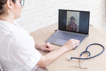 gp hosts an online appointment with an elderly quarantined patient at home. Female doctor at the desk talking to an elderly woman on a web camera and gives treatment recommendations