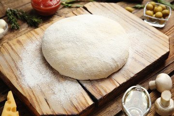 Dough and fresh ingredients for pizza on wooden table, closeup