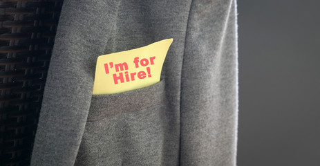 I'm for hire, words in red on a yellow paper stuck out from the pocket of a jacket.,