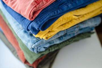 Neatly folded pants and jeans in bright colors on a white shelf. - obrazy, fototapety, plakaty