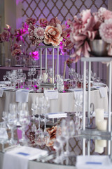 in the white hall of the restaurant there are tables with festive decor for a wedding celebration, decoration of the hall with fresh flowers, there are long white candles on the tables,