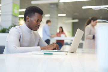 Side view portrait of young African-American man using laptop at work, copy space