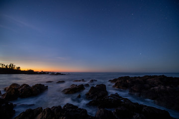 Fototapeta premium Ocean surf streams over black rocks at sunrise.