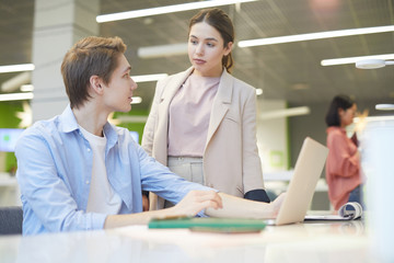 Portrait of young man explaining work project to female colleague while using laptop in office, copy space