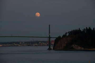 Moon rises over the Lion's Gate Bridge and Stanley Park in Vancouver, BC, Canada at dusk.