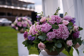 a large vase of flowers stands on a white pedestal in the park, a wedding decoration, a festive decor on the nature, pink flowers in a lush bouquet