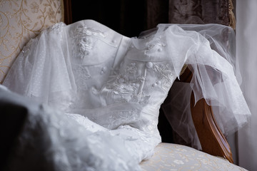 Fototapeta na wymiar white textured wedding dress lies on a chair by the window, the bride?s fees, the wedding morning before the wedding