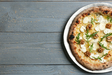 Delicious cheese pizza with walnuts and arugula on grey wooden table, top view. Space for text