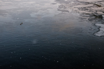 blue water on a river in winter, water freezes in the lake, snowflakes fly in the air, view from above ,