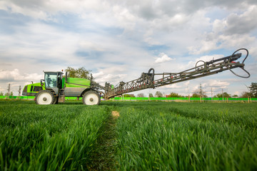 Tractor spraying pesticides, fertilizing on the vegetable field with sprayer at spring, fertilization concept