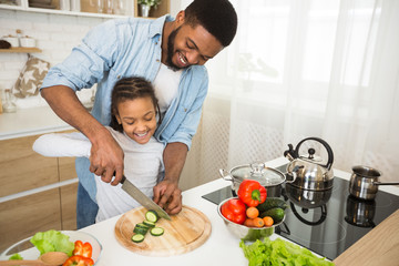 Dad teaching little daughter how to cut veggies