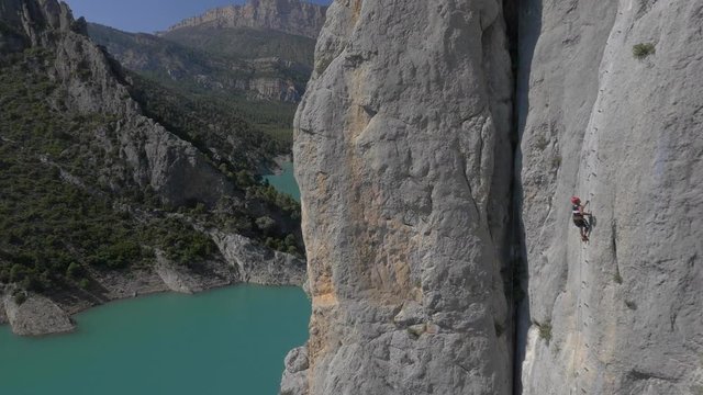 AERIAL DRONE SIDE SHOT DISCOVERING 1 PERSONS CLIMBING A MOUNTAIN WALL OVER STUNNING VALLEY AND RESERVOIR